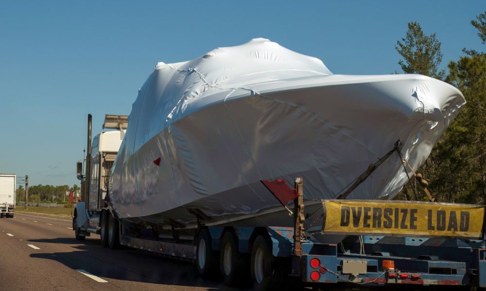 A yacht is wrapped up in a white tarp and attached to a trailer that is connected to a semi-truck.